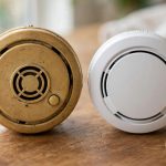 photo of an old yellowed smoke detector next to a brand-new white one on a wooden table, side-by-side comparison, soft daylig